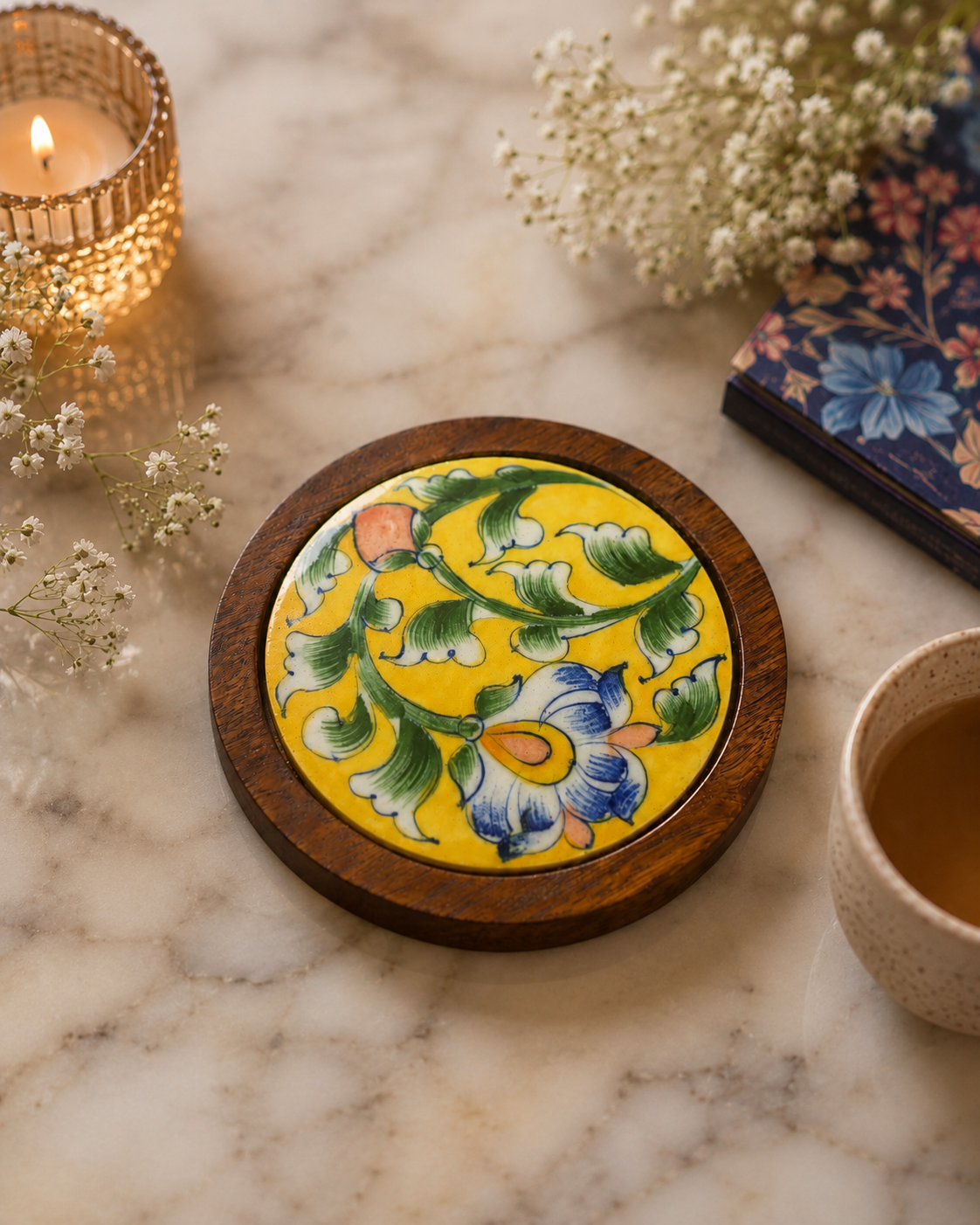 Decorative coaster with floral design on a marble surface with a candle and flowers.