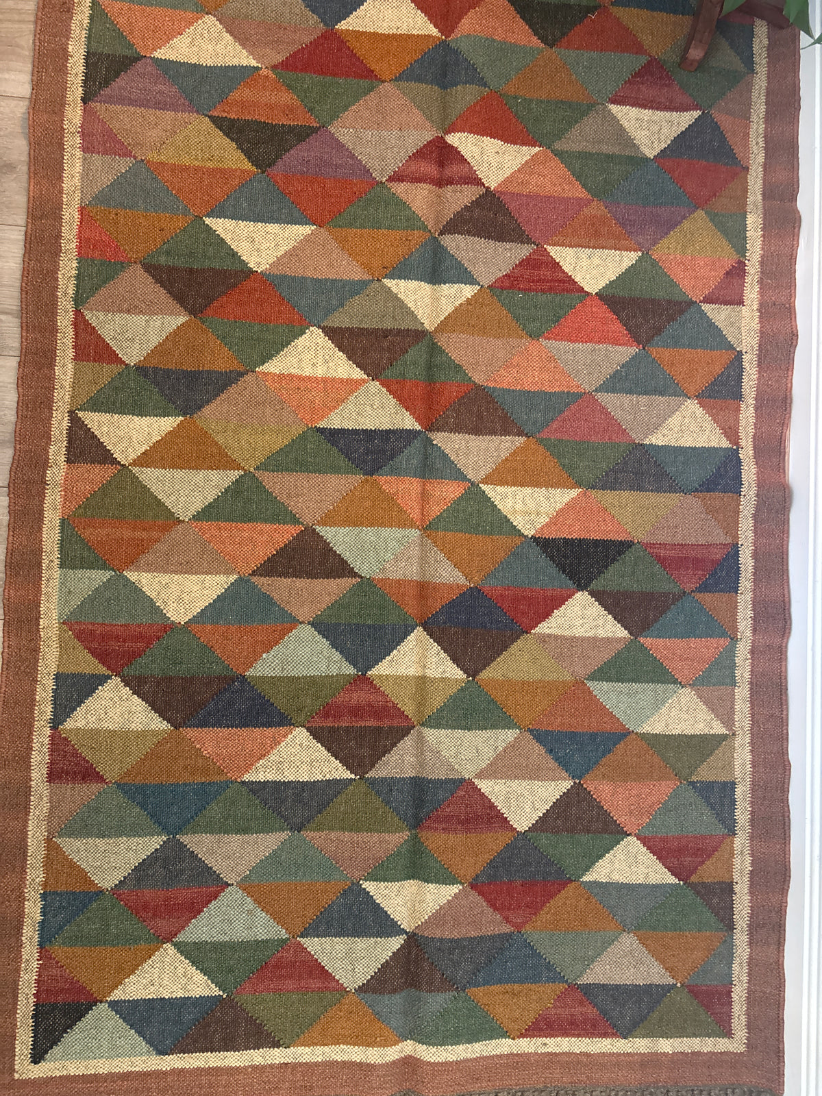 Geometric patterned rug with triangle shapes in earthy tones on a wooden floor.