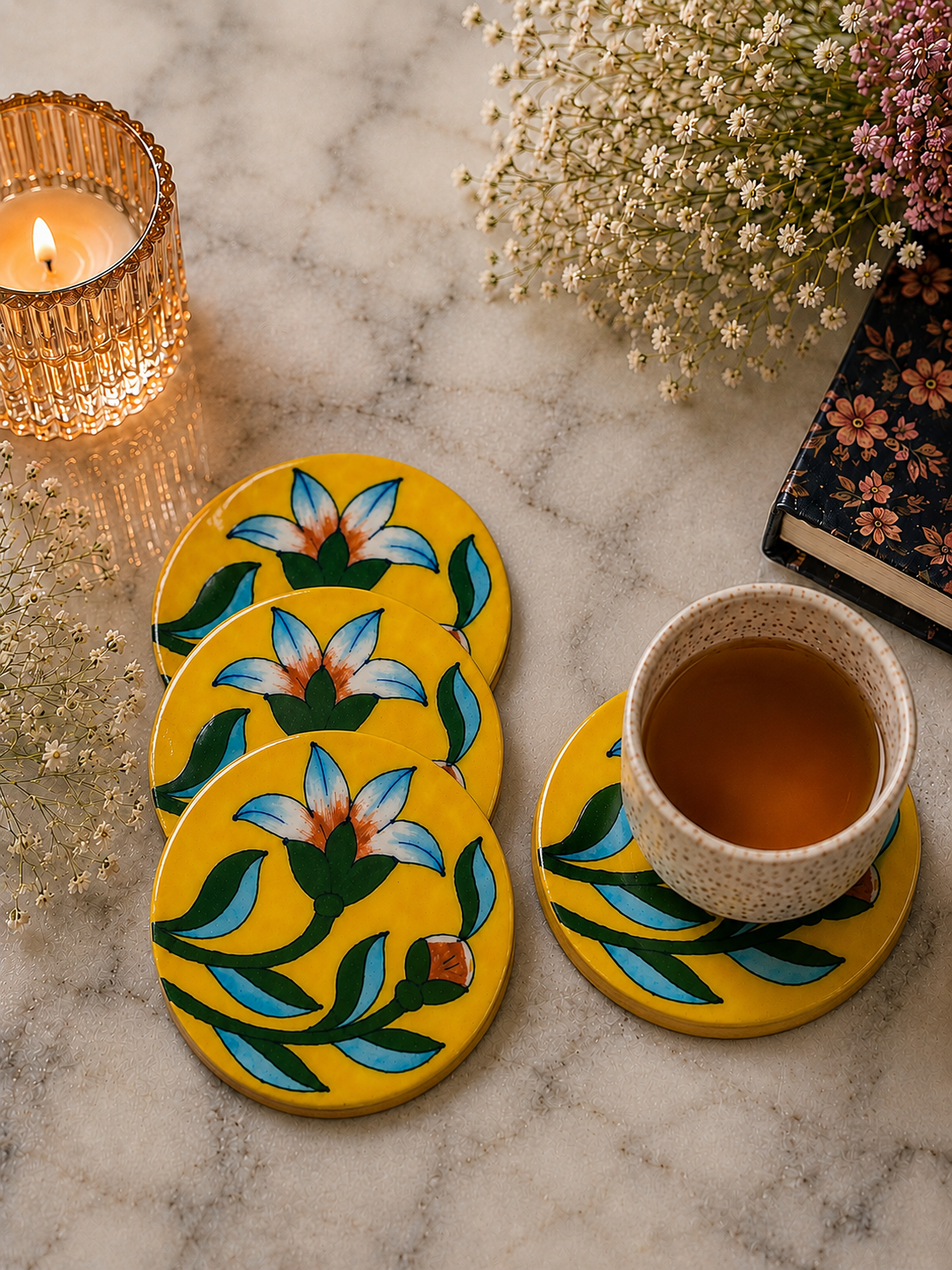 Set of four floral coasters on a marble surface with a cup of tea and decorative elements.
