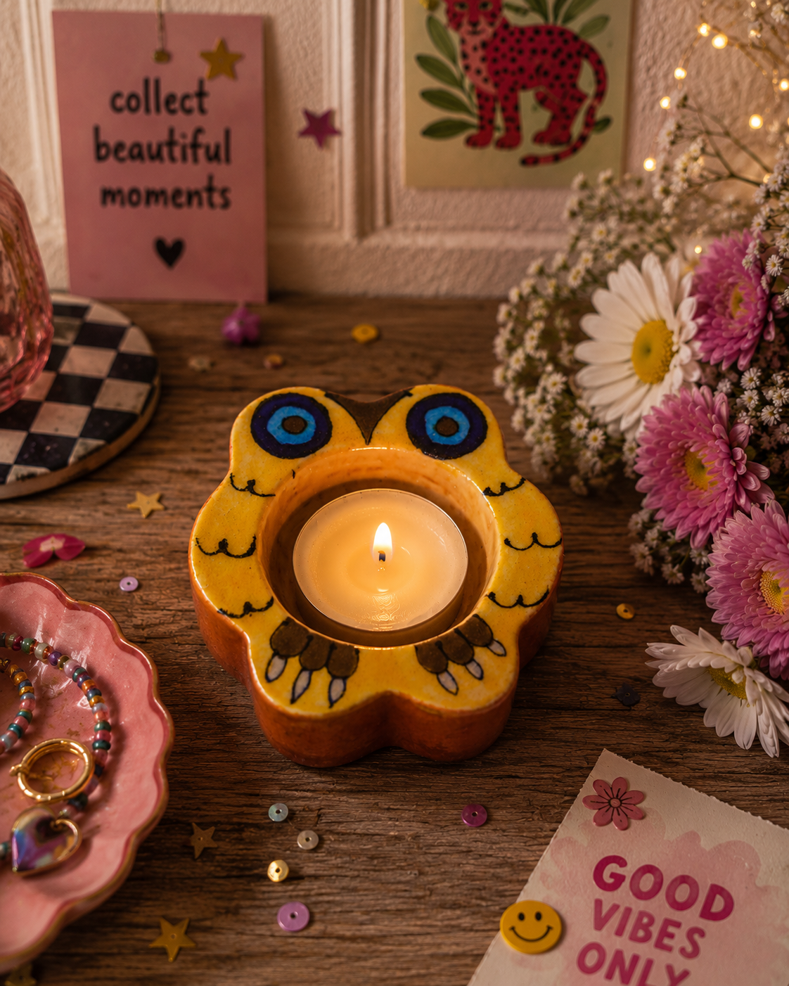 Candle in an owl-shaped holder on a wooden surface with decorative elements.
