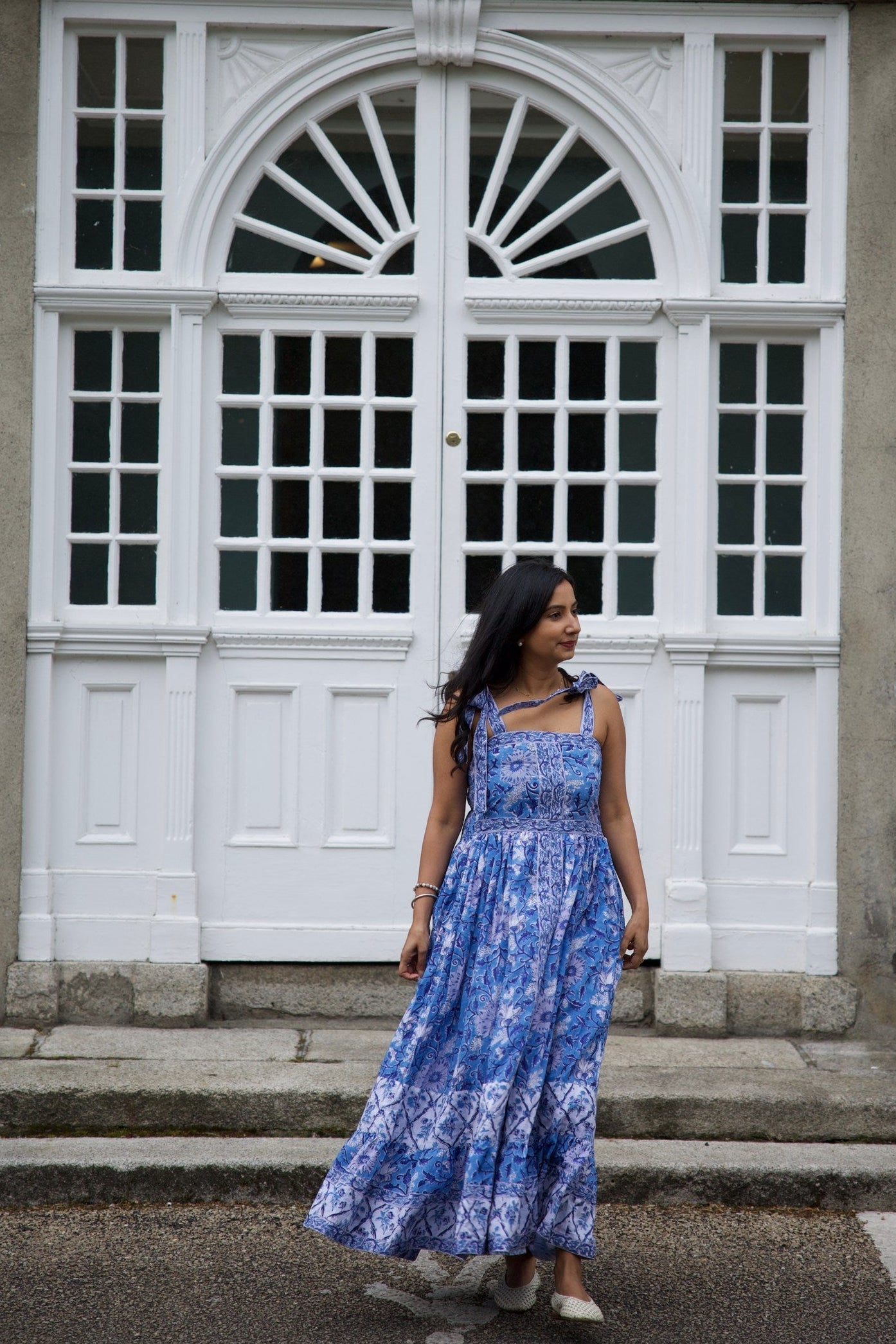 Woman in a blue dress standing in front of a white door with glass panels.