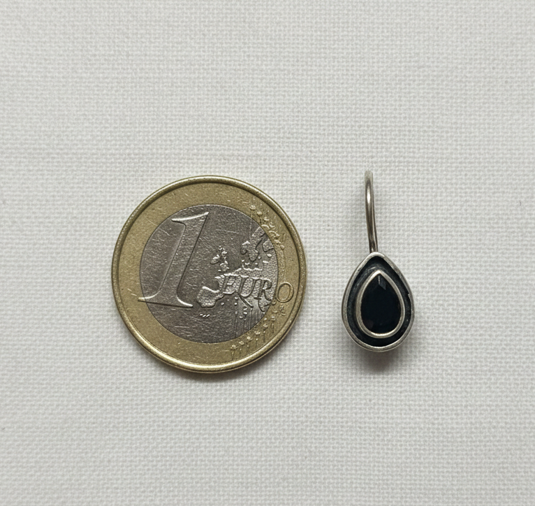 Teardrop-shaped earring next to a one Euro coin on a light gray background