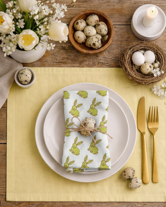 Easter table setting with bunny-themed napkin, eggs, and flowers on a wooden table.