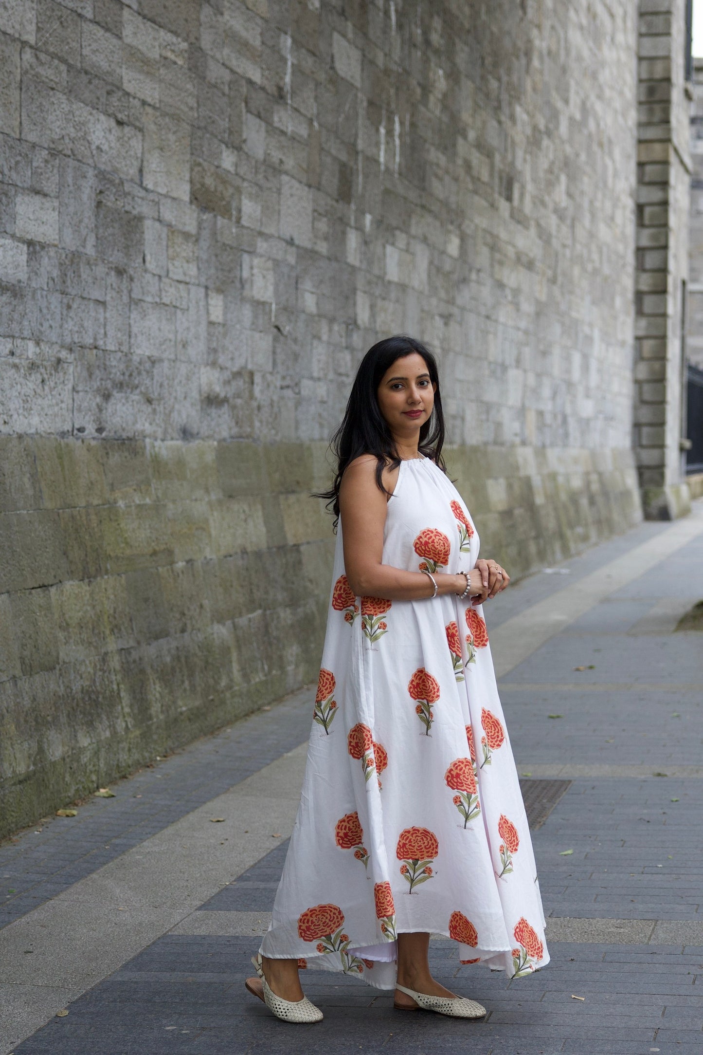 Woman in a white dress with red floral patterns standing on a sidewalk.