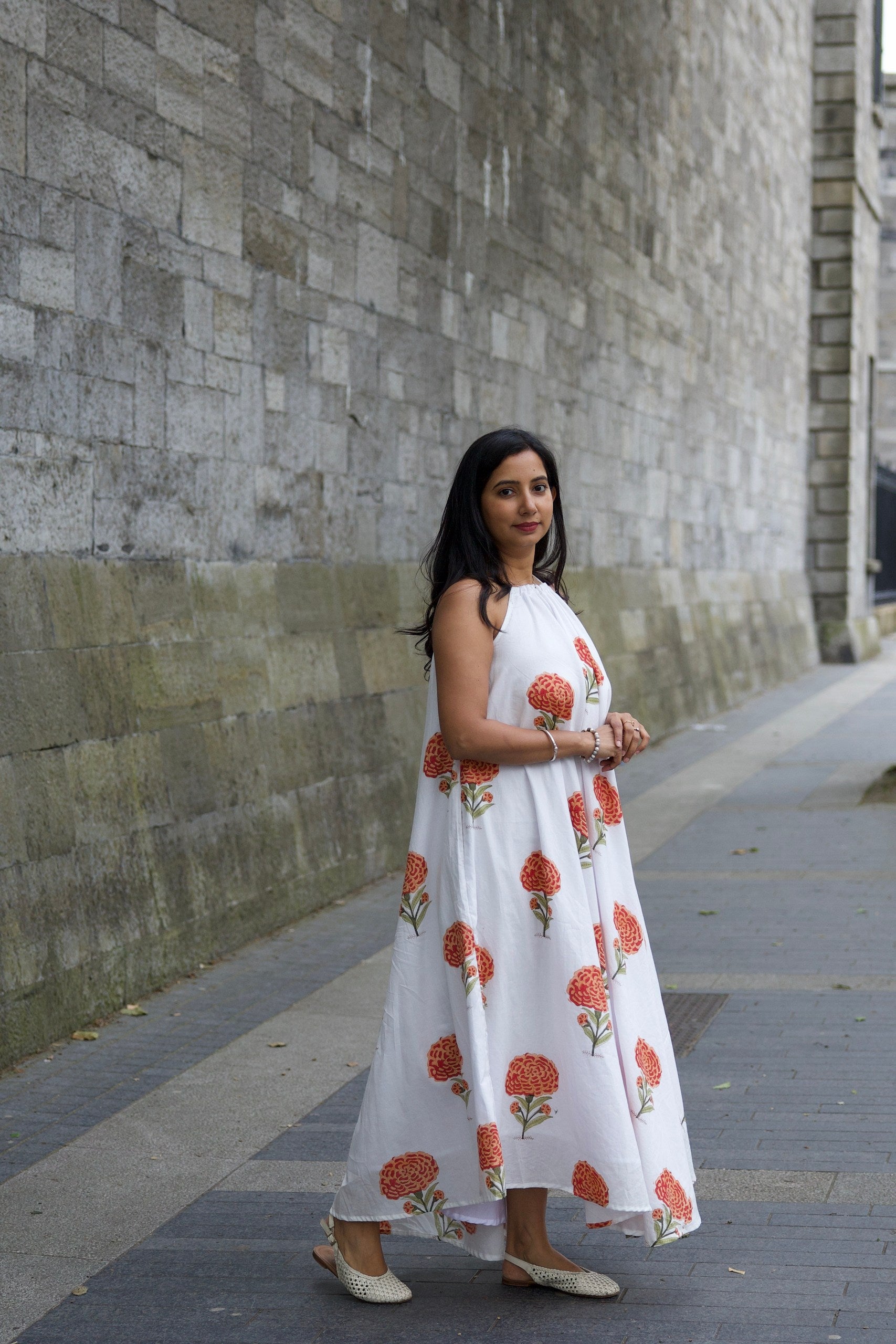 Woman in a white dress with red floral patterns standing on a sidewalk.