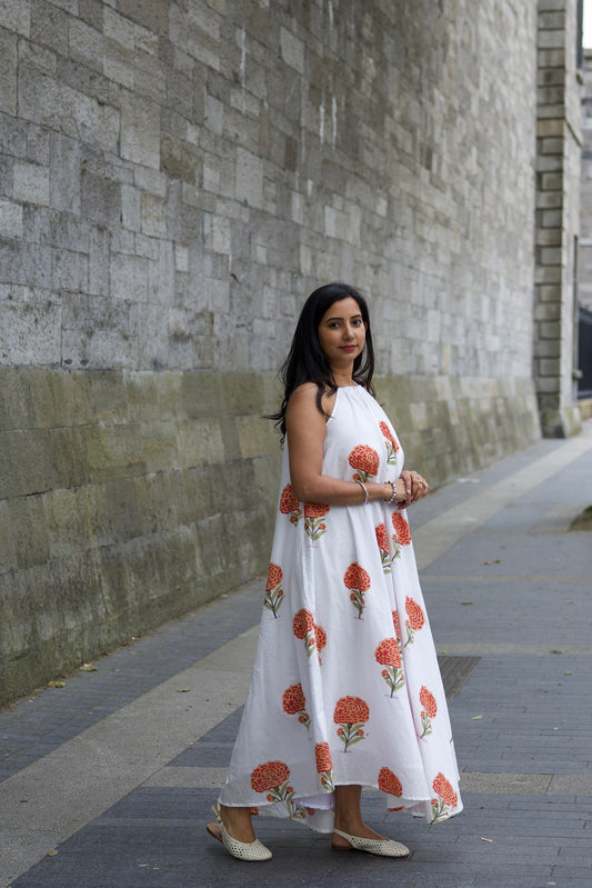 Woman in a white dress with red floral patterns standing on a sidewalk.