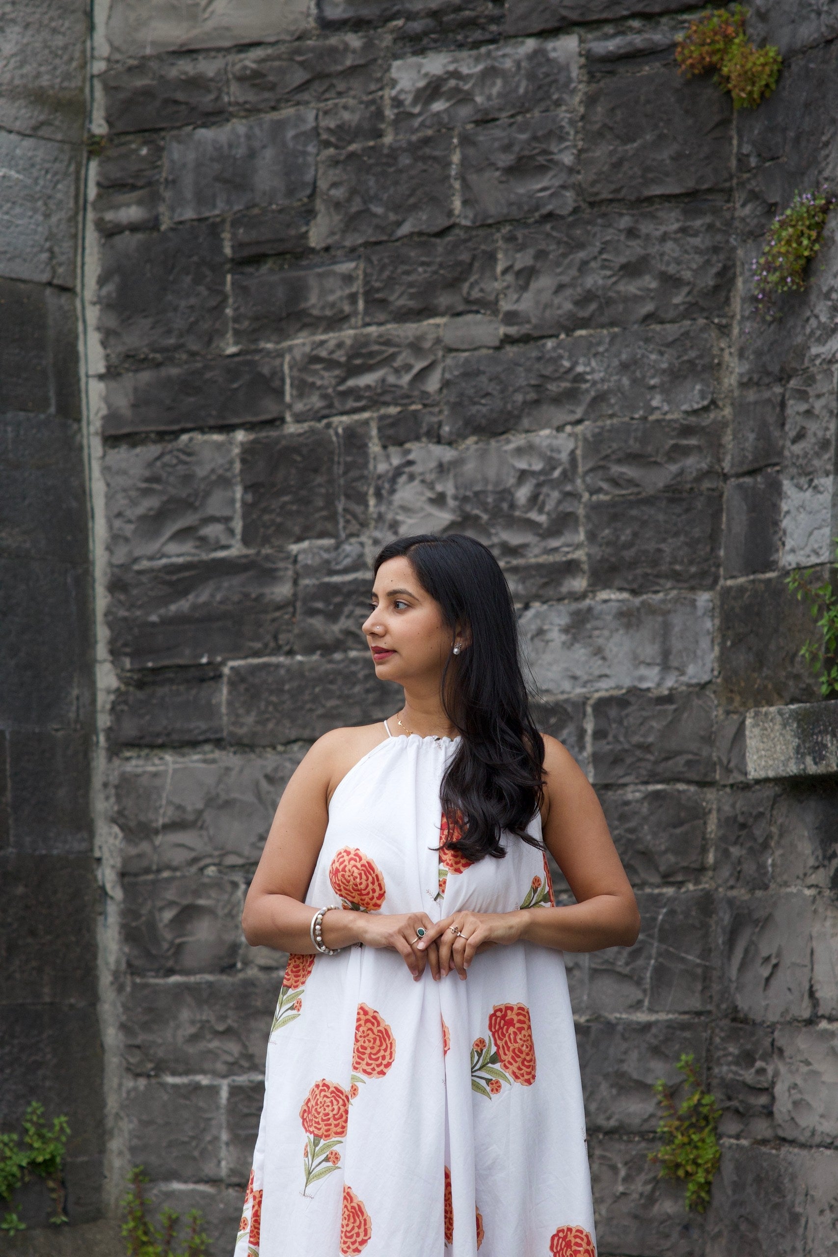 Woman in a white dress with red patterns standing against a stone wall.