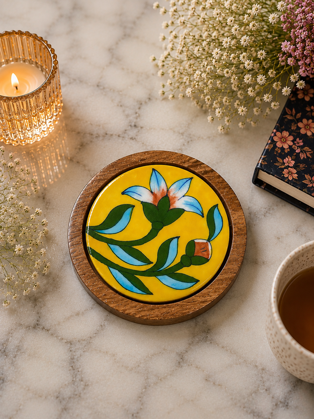 Decorative coaster with floral design on a marble surface with a candle and flowers.