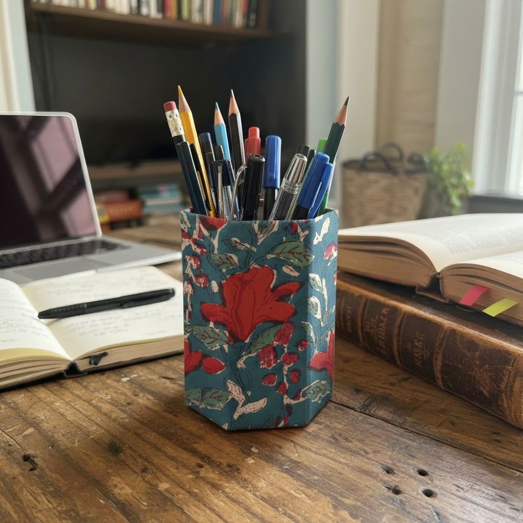 Floral-patterned pen holder with pens on a desk with books and a laptop.