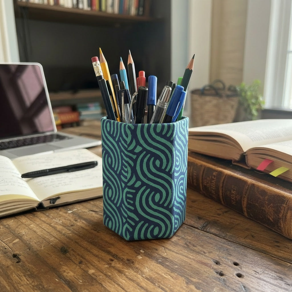 Pencil holder with pens on a desk with books and a laptop in the background